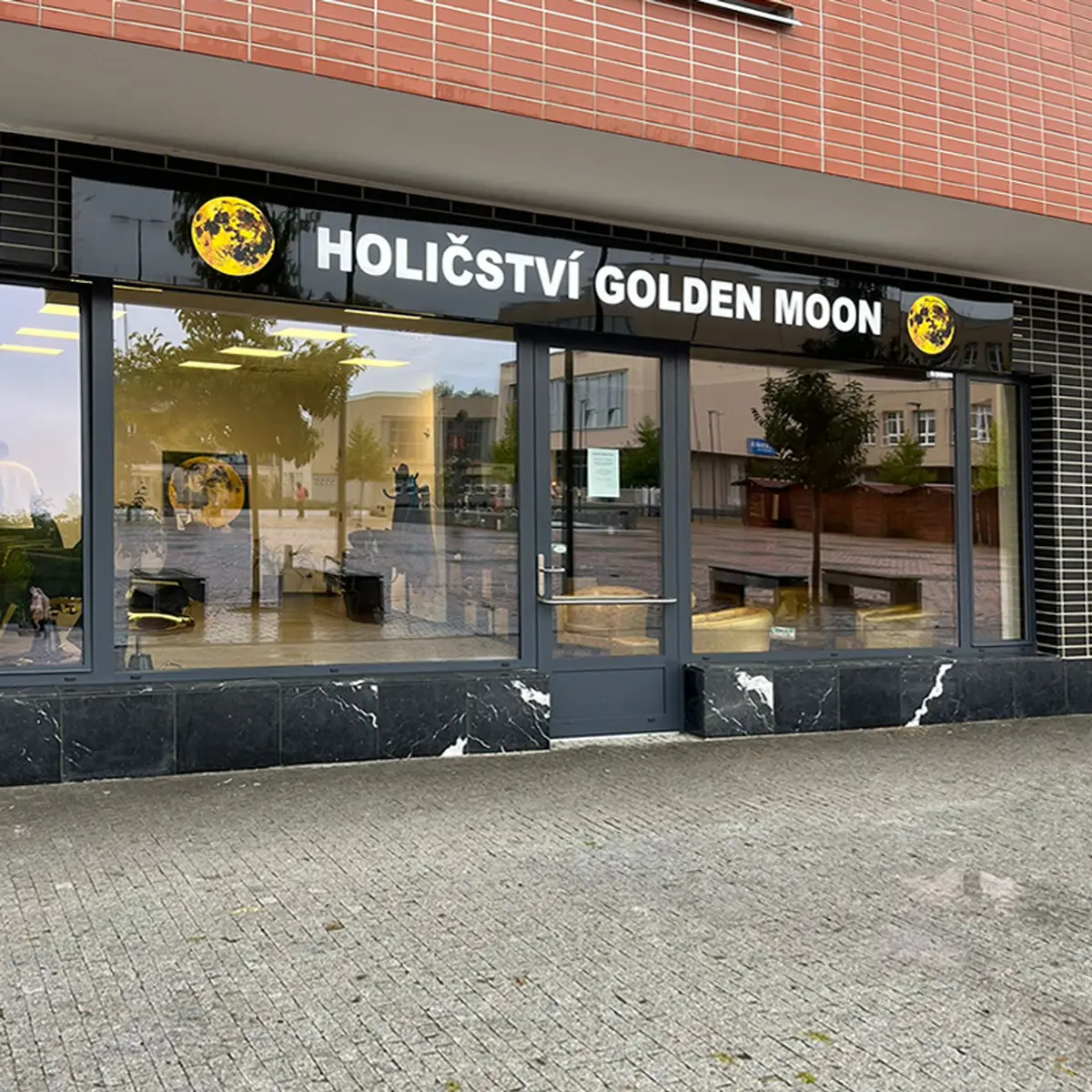 Světelné reklamní boxy a logo Golden Moon na fasádě holičství